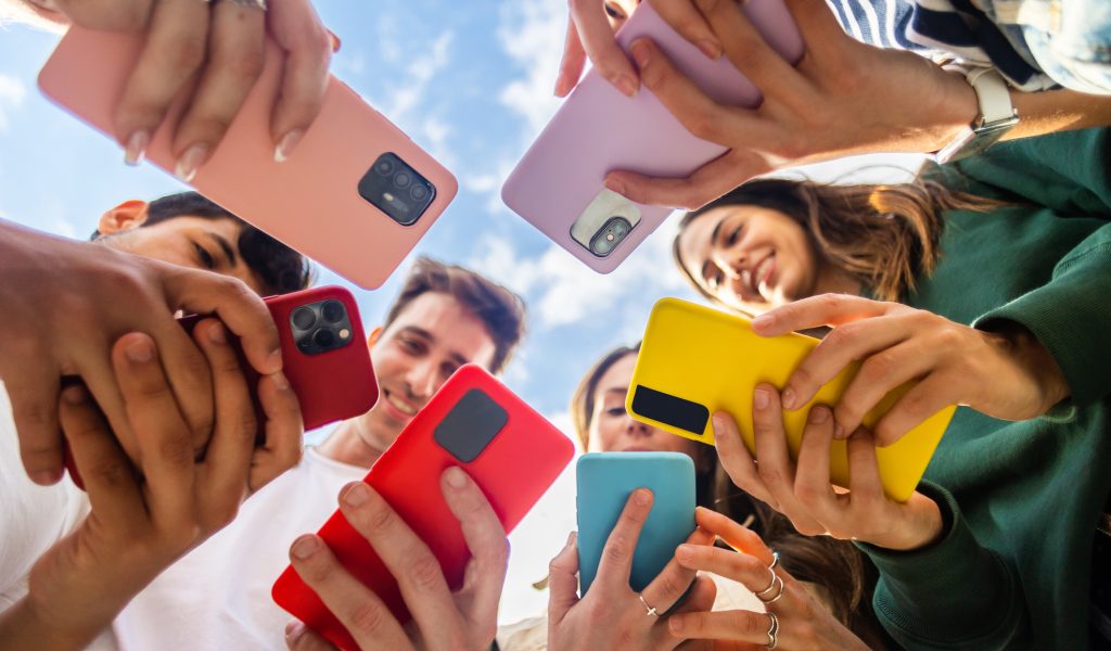 A diverse group of Gen Z individuals holding smartphones in a circle, symbolizing their digital-native lifestyle and strong connection to mobile technology.