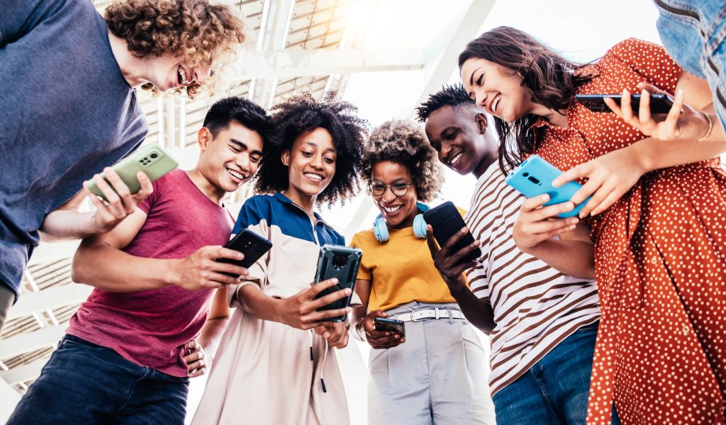 A diverse group of Gen Z individuals smiling while using smartphones, emphasizing the need for personalized, mobile-first financial products from credit unions.